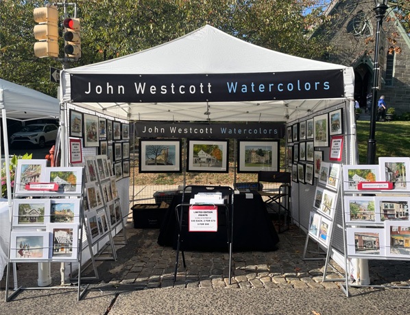 Vendor booth with hanging banner, art grid panels, and A-frame signage